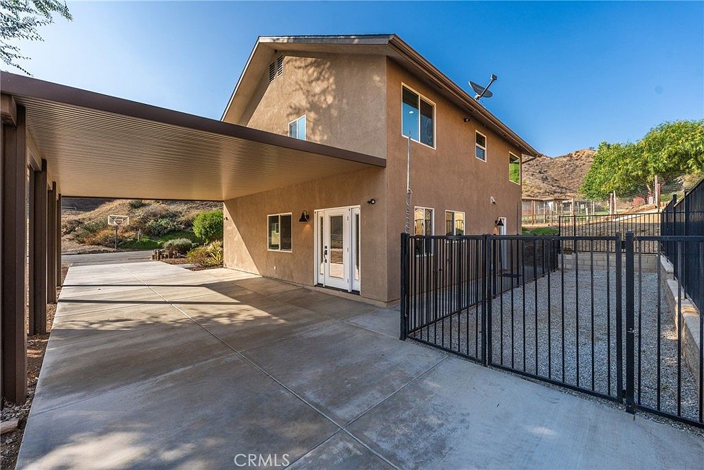 Stucco exterior with covered carport and access to back patio, canyon beyond fence