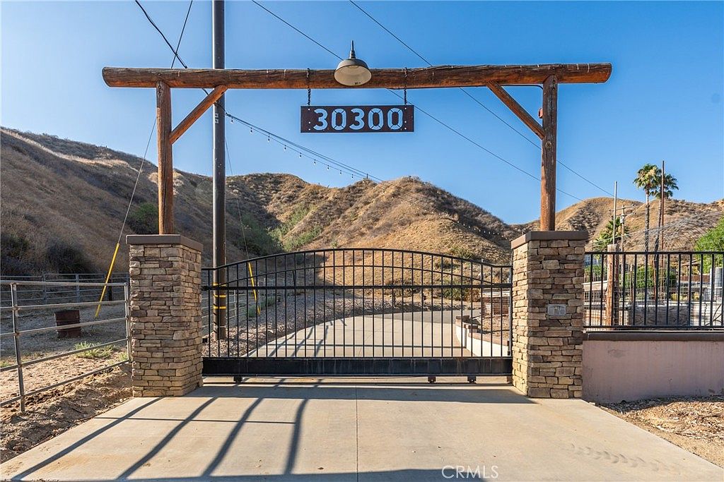 Wooden ranch gate marked 30300 with stone pillars opening onto the Live Oak Canyon drive, Redlands hills beyond.